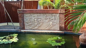 A decorative wall with relief sculptures, a small pond with lily pads, and a traditional clay pot. - Tropical pool villa, perfect for big families, group getaways & family reunions (Tambon Rawai)