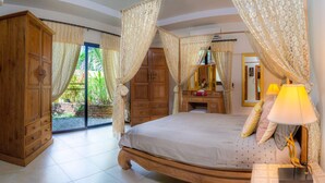 A bedroom with a bed, a wooden wardrobe, a mirror, a lamp, and a view of a garden through a glass door. - Tropical pool villa, perfect for big families, group getaways & family reunions (Tambon Rawai)