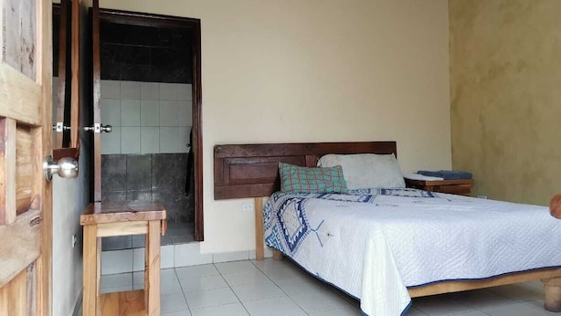 A bedroom with a wooden bed, a nightstand, a small wooden table, and a door leading to a bathroom.
