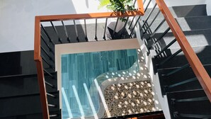 A modern indoor space with a glass-bottomed staircase, a pool area, and a seating arrangement with two wicker chairs and a table. - Mint Hoi An Villa (Da Nang)