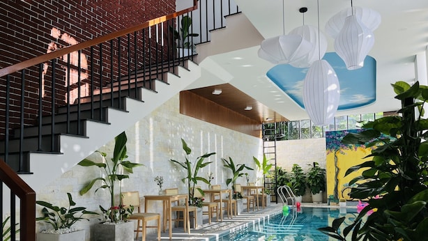 A modern indoor pool area with a staircase, seating, and plants. - Mint Hoi An Villa (Da Nang)