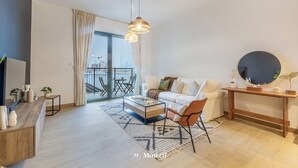 A modern living room with a sofa, coffee table, and a round mirror on a console table. - Manzil - 1BR | Near La Mer Beach | Pool & Sea View (Dubai)