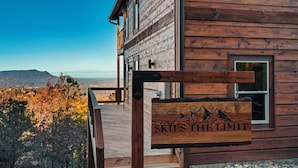 A wooden cabin with a sign reading "SKIES THE LIMIT" and a view of mountains in the background.
