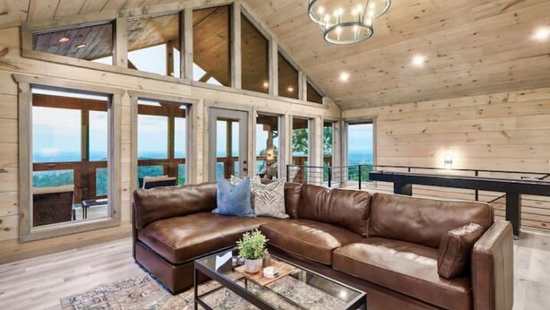 A spacious living room with a large brown leather sofa, a glass coffee table, and a chandelier.