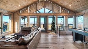 A spacious living room with a high ceiling, large windows, a fireplace, and a staircase leading to an upper level.