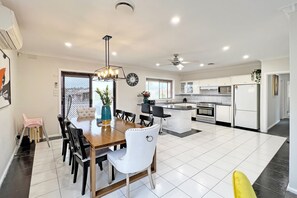 Une cuisine moderne avec des meubles blancs, un îlot central et un coin repas comprenant une table et des chaises en bois.