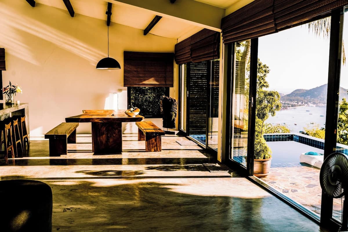 A modern interior with a wooden dining table, benches, and a large window overlooking a scenic view.