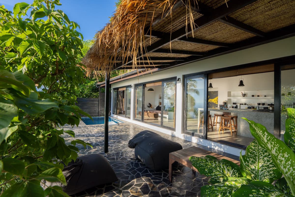 A modern house with a glass-enclosed kitchen, a pool, and outdoor seating.