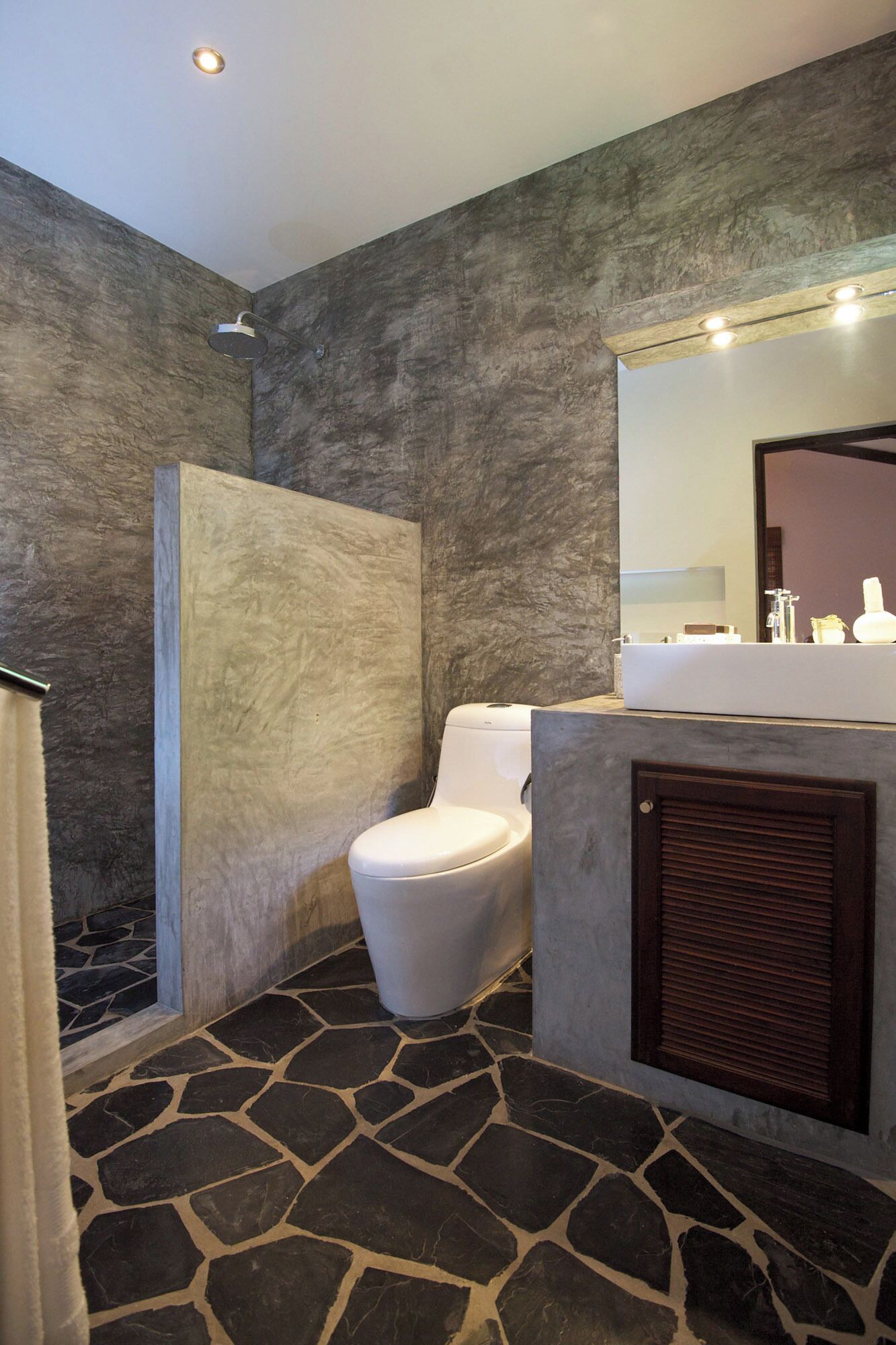 A modern bathroom with a stone floor, a shower, a toilet, and a vanity with a mirror.