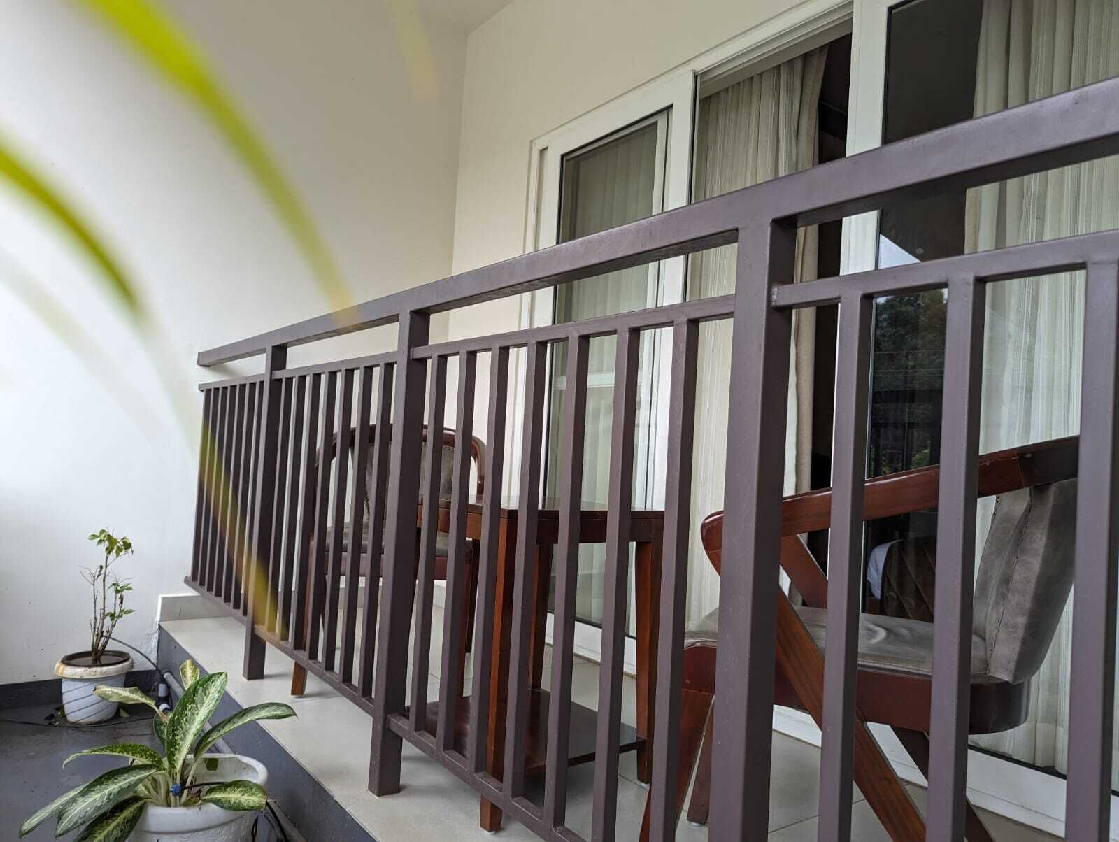 A balcony with a metal railing, potted plants, and a view of the interior through the windows.