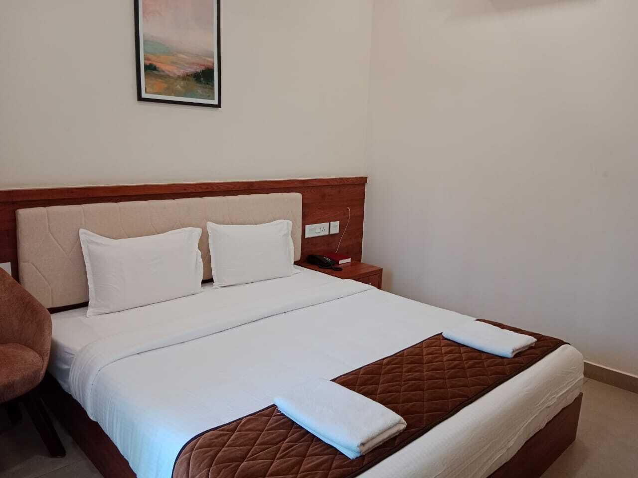 A hotel room with a large bed, a wooden headboard, a bedside table with a phone, and a painting on the wall.