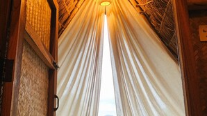 Una entrada con cortinas blancas que da a una vista de un campo verde y montañas.