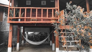 Una casa de madera con balcón, una hamaca y un pequeño jardín.