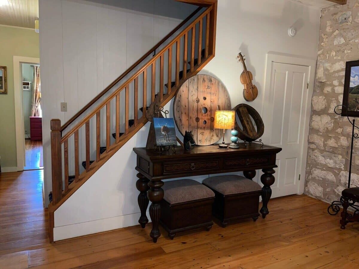 Een trap met houten leuningen, een houten tafel met een lamp, en een viool aan de muur.