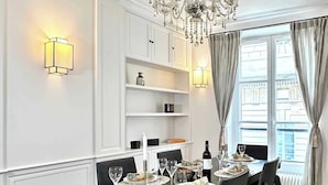 A dining room with a chandelier, white walls, and a window with curtains.