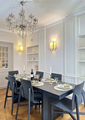 A dining room with a large table set for six, elegant chairs, a chandelier, wall sconces, and built-in shelving.