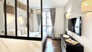 A modern hotel room with a bed, a dresser, a mirror, and a window with curtains.