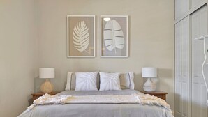 Une chambre à coucher comprenant un lit, deux tables de chevet, deux lampes et deux œuvres d’art représentant des feuilles, encadrées et accrochées au mur.