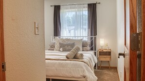 Ein Schlafzimmer mit Bett, Nachttisch, Fenster mit Vorhängen und einer Tür.