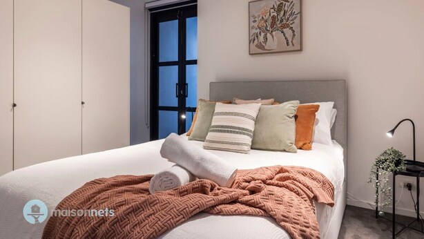 Une chambre à coucher avec un lit, des oreillers, une couverture, une porte et une œuvre d’art décorative au mur.