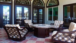 A patio area with a round table and four cushioned chairs, large arched windows, and a tiled floor. - Remodeled Gem - Comfort and Location (Kissimmee)