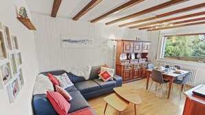 Una sala de estar acogedora con un sofá azul, una mesa de comedor de madera y vistas al exterior a través de un amplio ventanal.