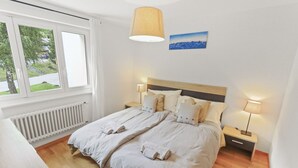 Un dormitorio con una cama grande, dos mesitas de noche, una ventana con vistas y un cuadro en la pared.
