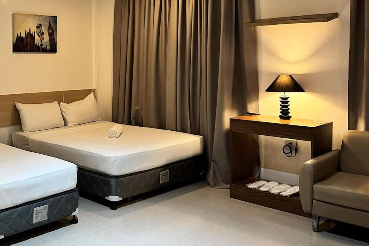 Habitación de hotel con dos camas, una mesita de noche con lámpara, una silla y un cuadro en la pared.