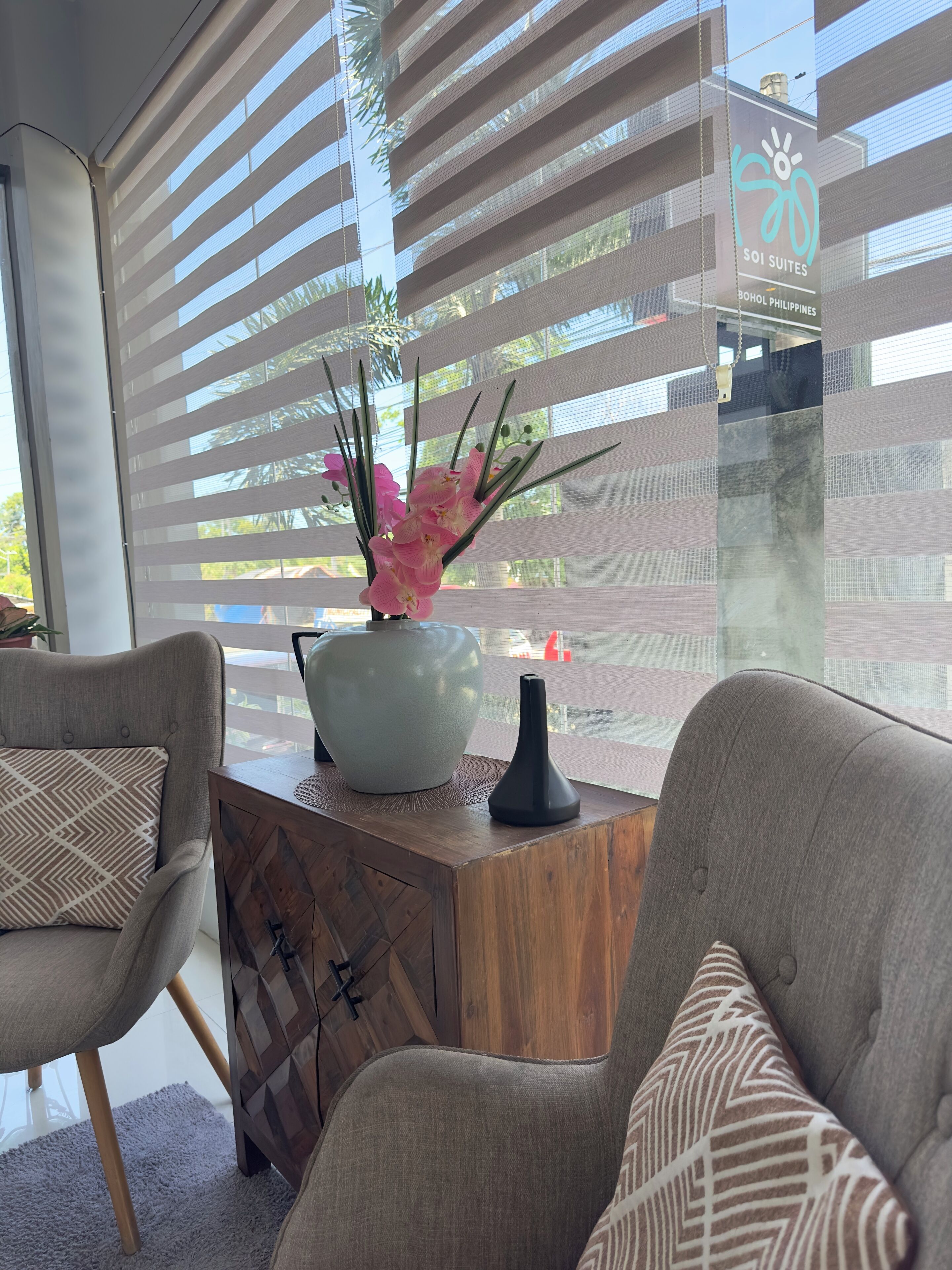A modern living room with a sofa, a coffee table, and a vase with pink flowers.