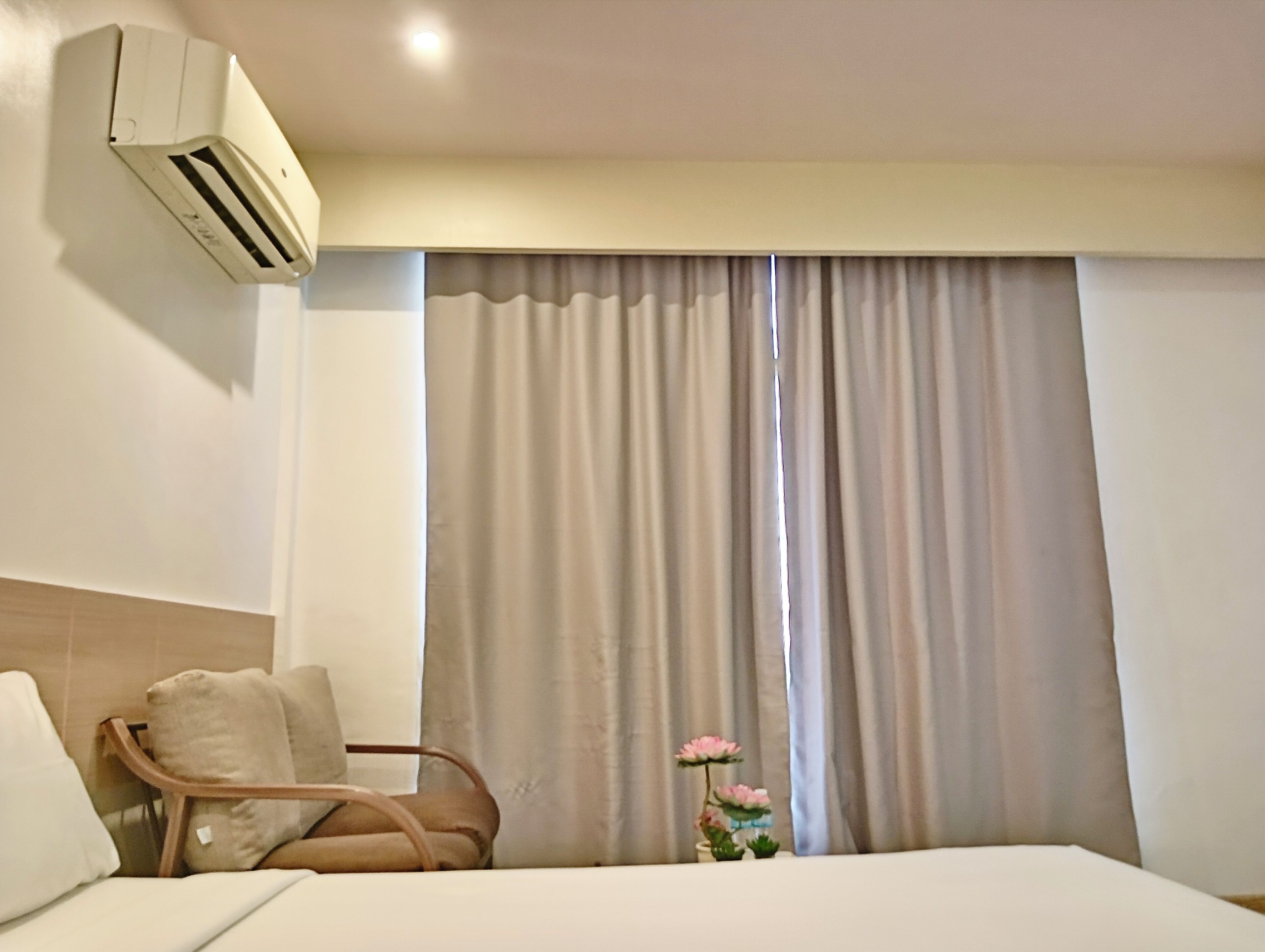 Een hotelkamer met een bed, een stoel, een airconditioning en een raam met gordijnen.