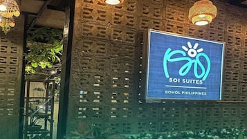 A hotel entrance with a sign for SOI Suites, a wooden wall with a lattice design, and hanging wicker lamps.