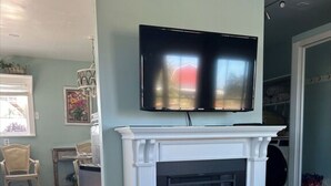 Una sala de estar con chimenea, un televisor montado encima y una mesa en primer plano.