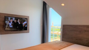 Habitació d'hotel amb un llit, televisió penjada a la paret i una finestra gran que ofereix vistes cap a l'exterior.