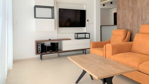 Un saló modern amb una taula de centre de fusta, un sofà, un televisor fixat a la paret i un moble d'entreteniment encastat.