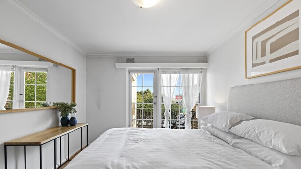 Een slaapkamer met een groot bed, een nachtkastje, een spiegel en uitzicht op het balkon.