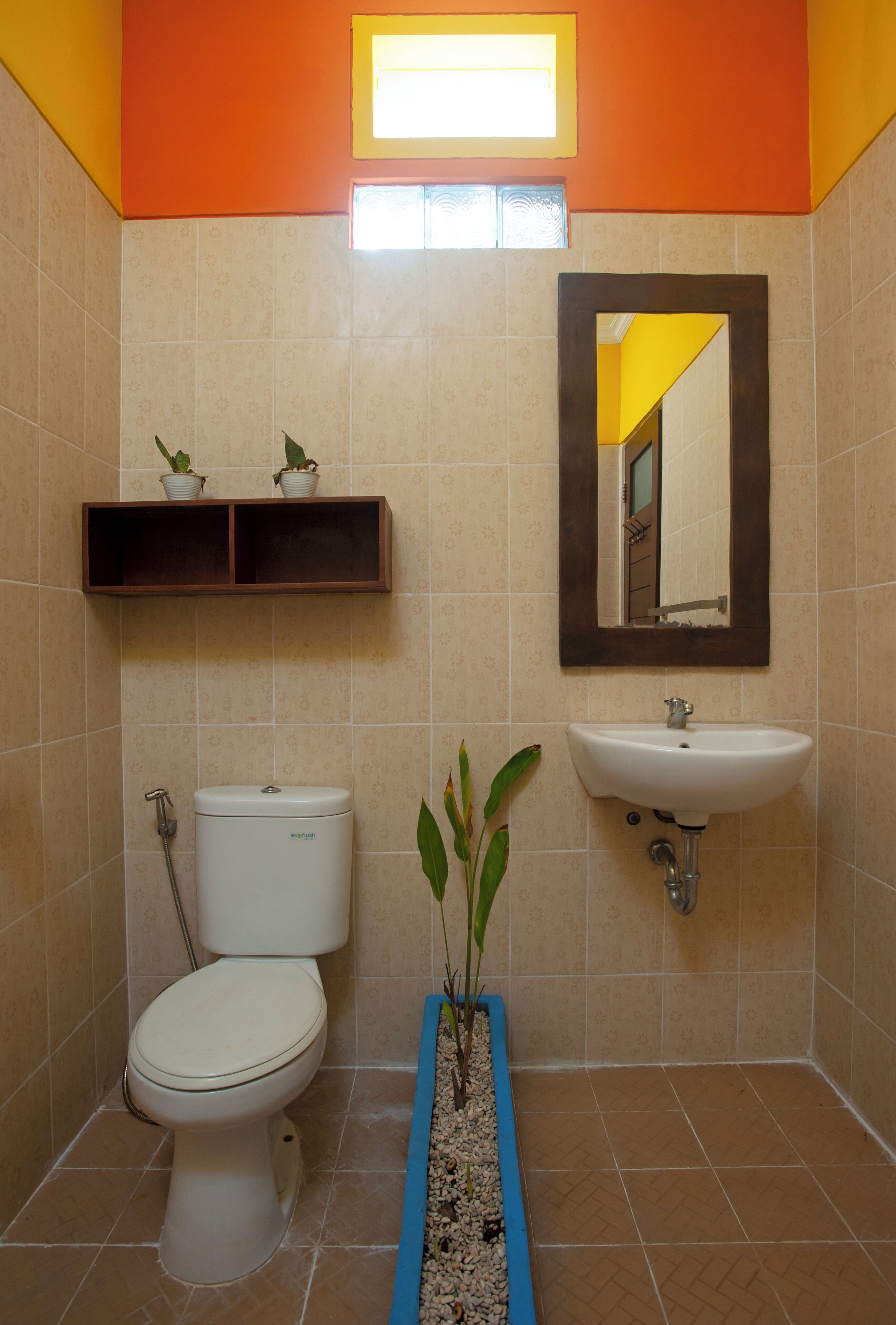 A bathroom with a toilet, sink, and mirror. There are two potted plants on a shelf above the toilet.