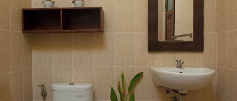A bathroom with a toilet, sink, and mirror. There are two potted plants on a shelf above the toilet.