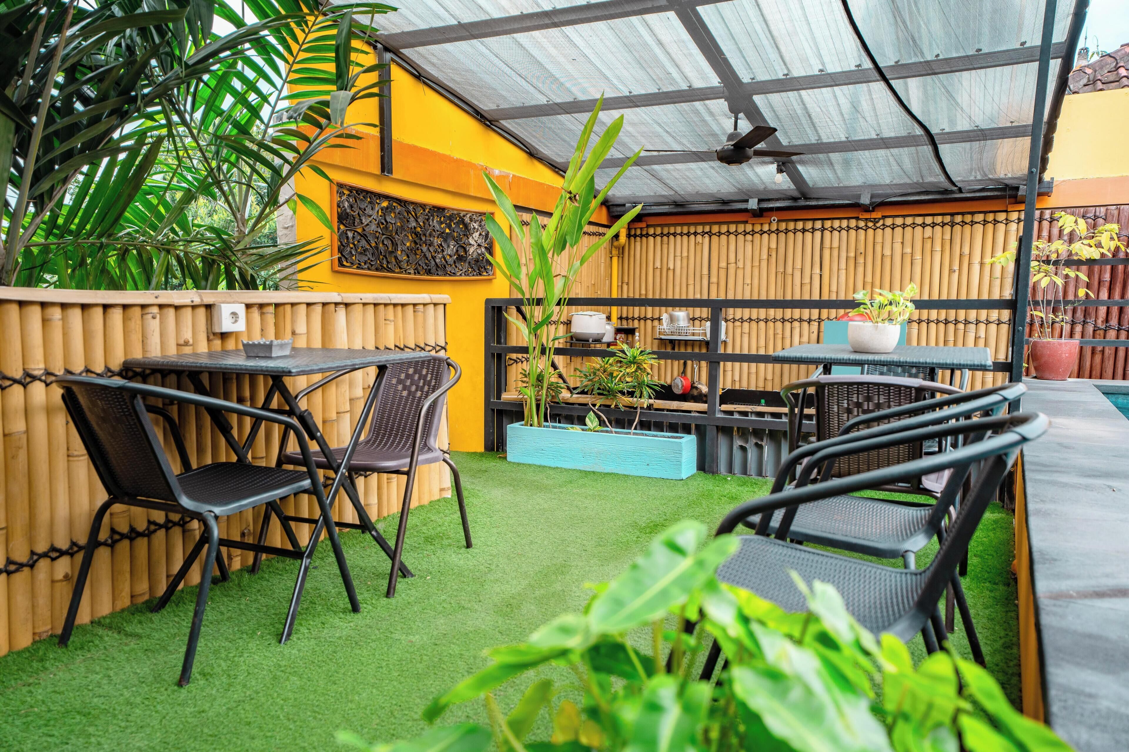 An outdoor patio with artificial grass, bamboo fencing, and black metal chairs.