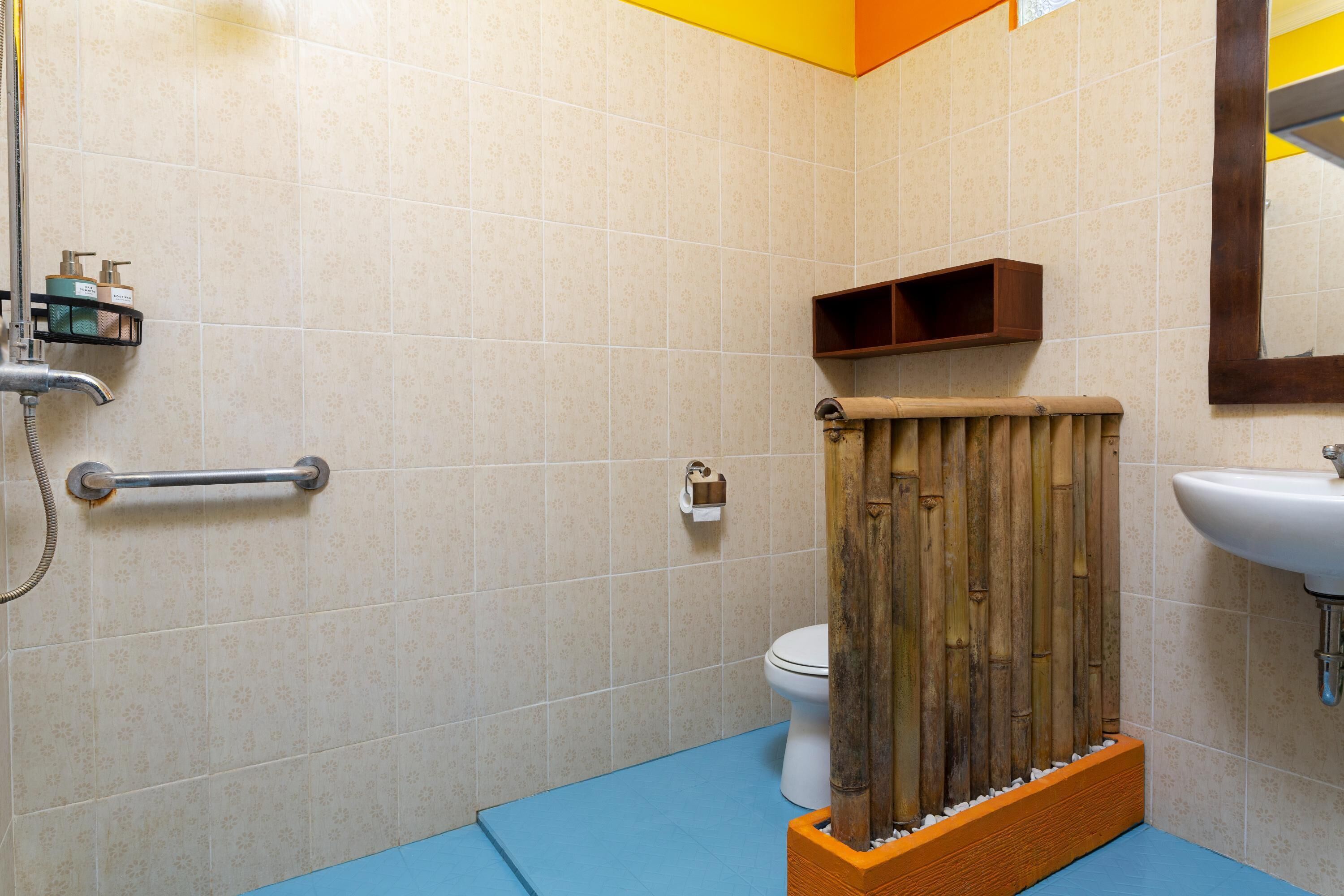Baño con inodoro, lavamanos, zona de ducha y separador de madera.