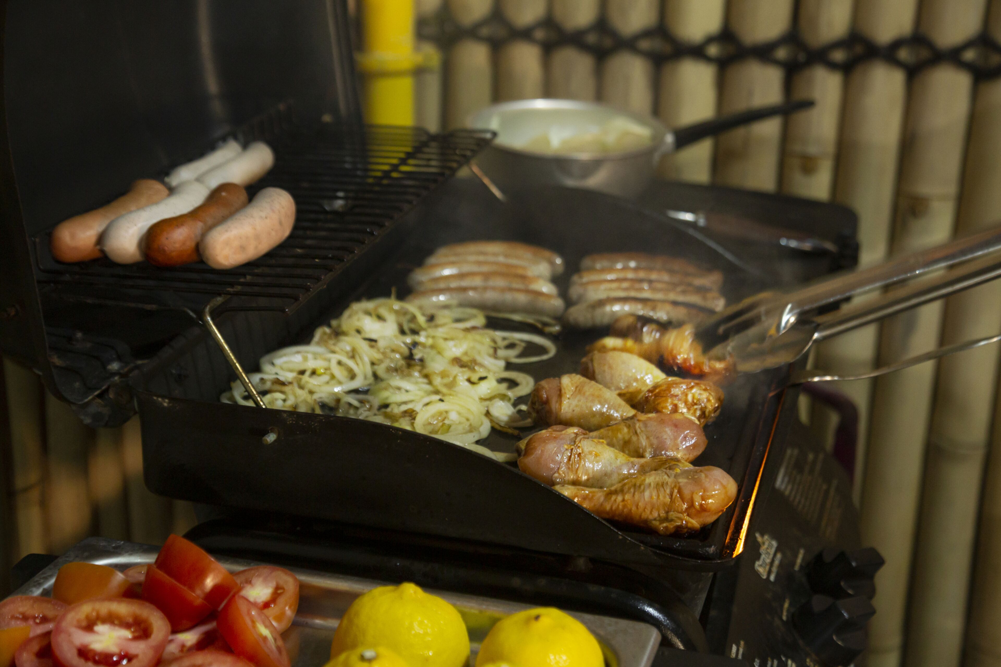 A grill with sausages, chicken, and onions being cooked.