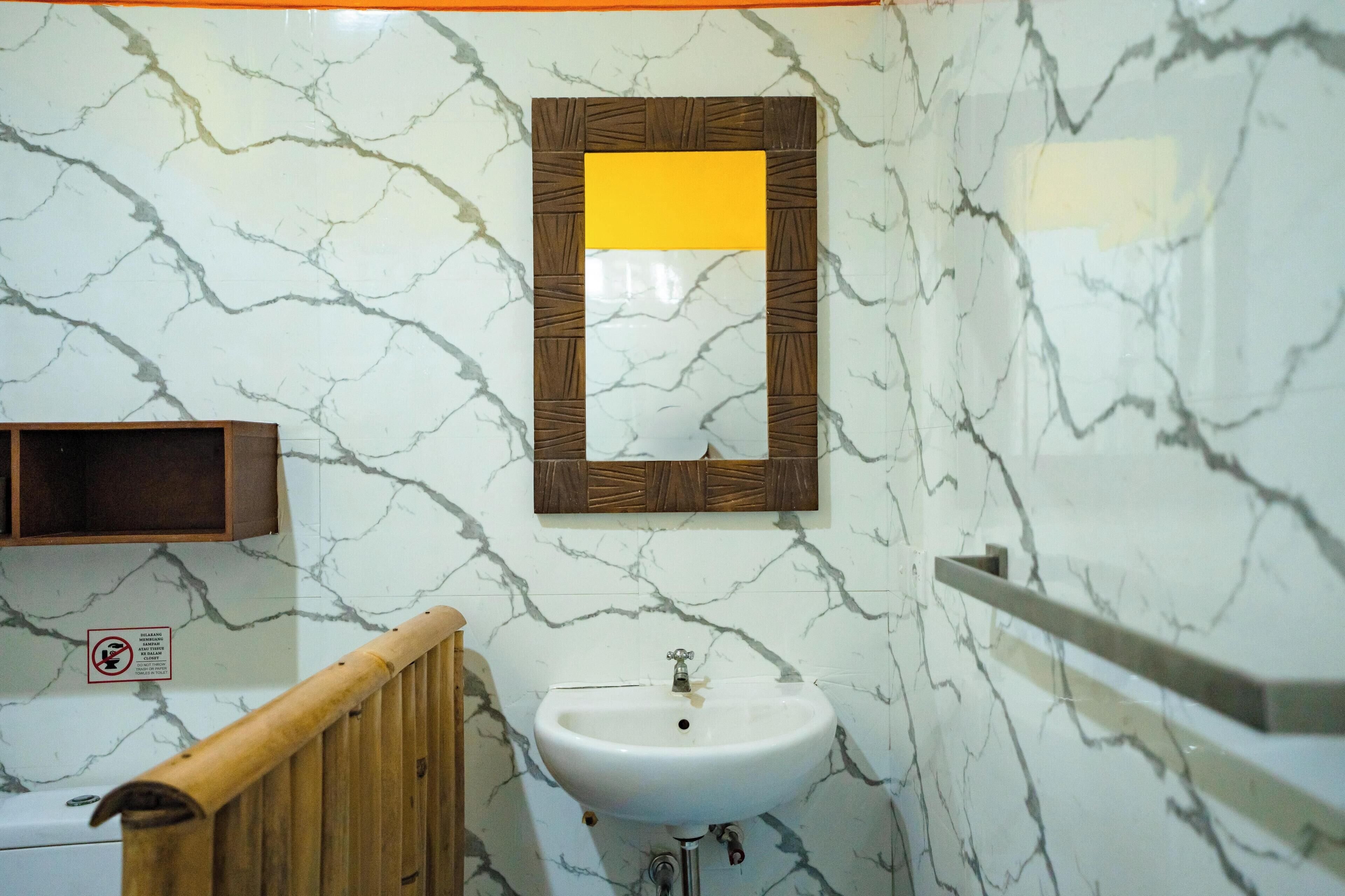 A bathroom with a marble wall, a white sink, a wooden handrail, and a mirror with a wooden frame.