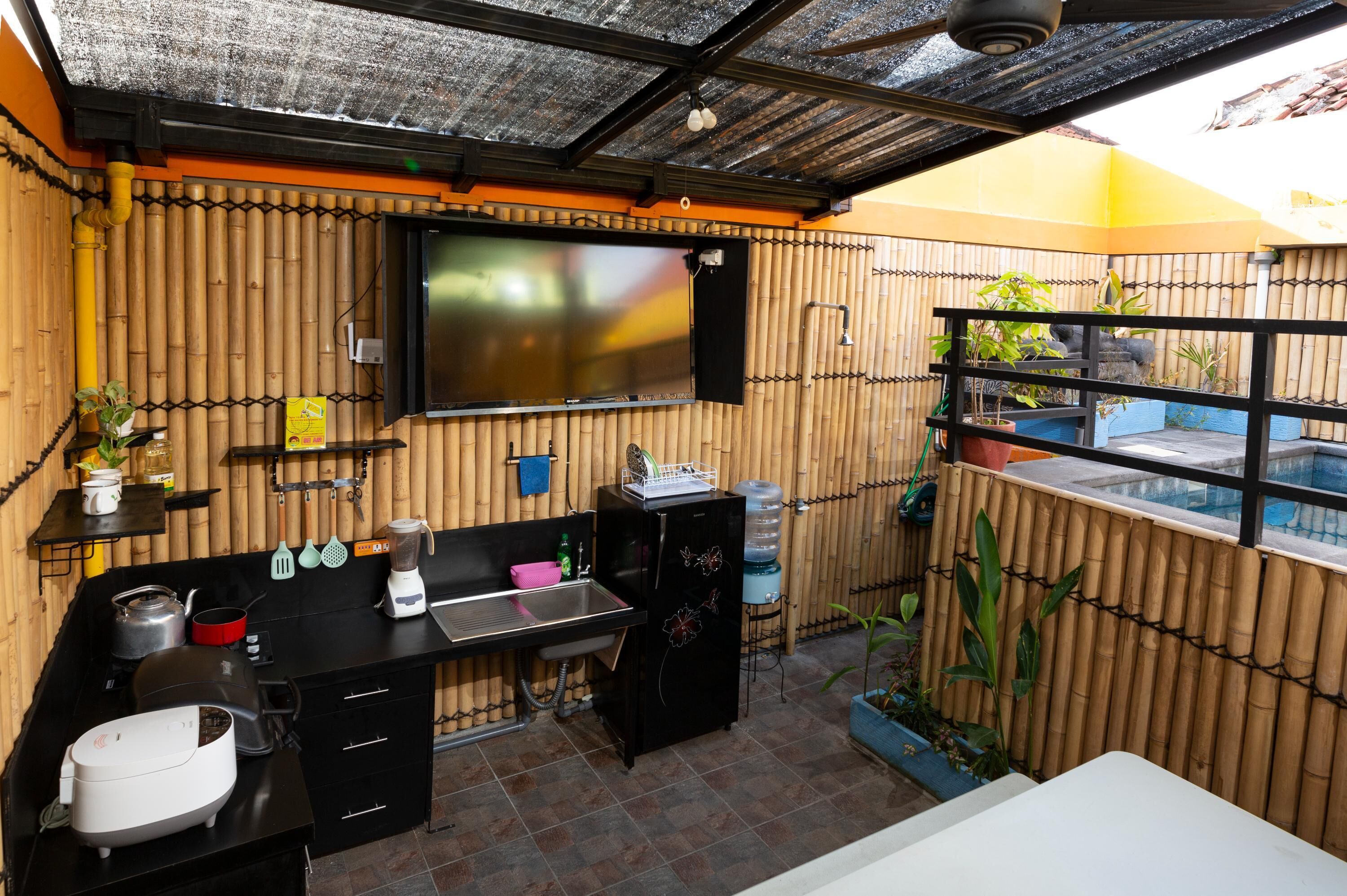 A compact kitchen with a black countertop, a sink, and a stove. There is a bamboo wall and a small window with a view of the outside.