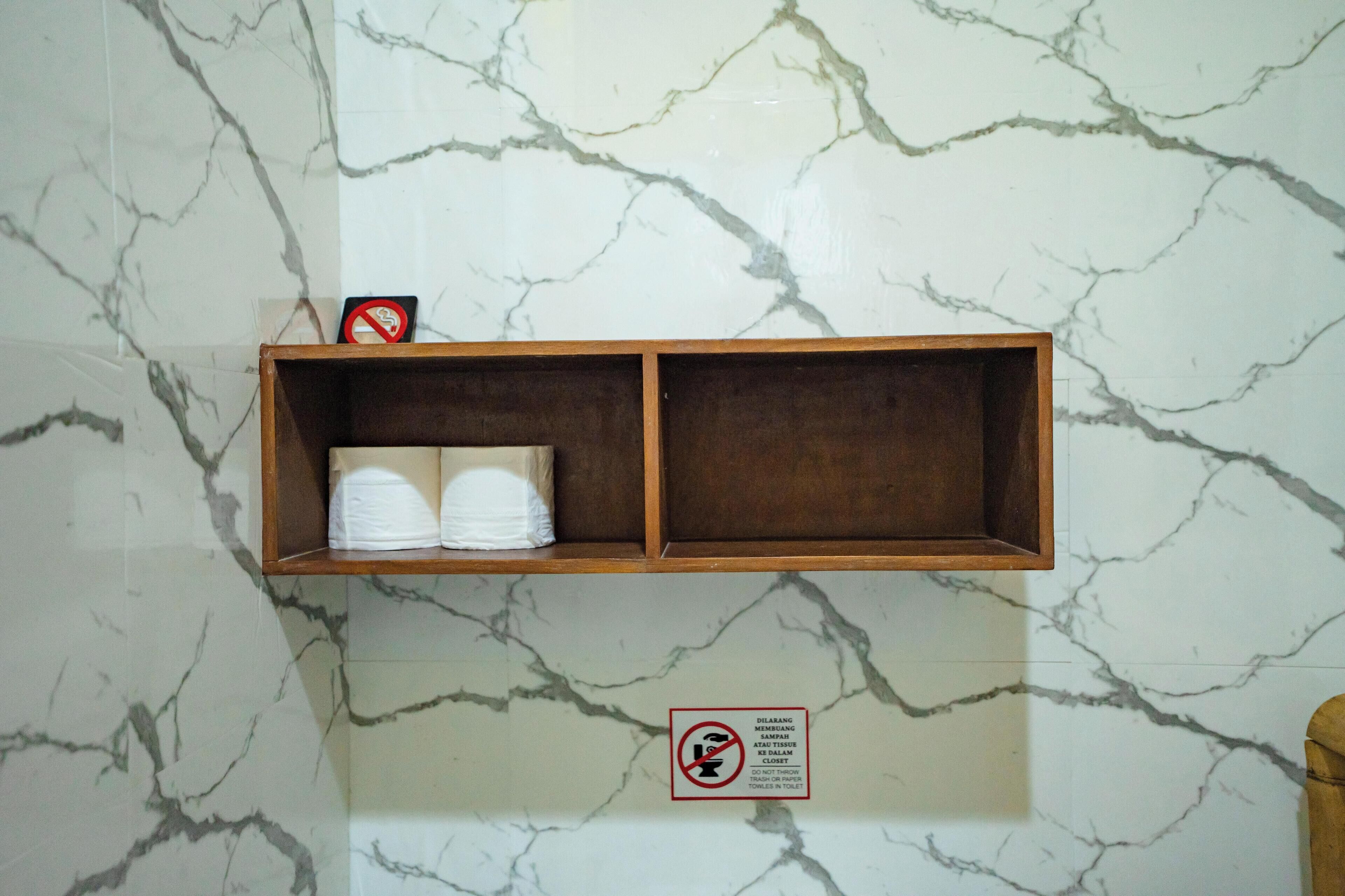A marble wall with a wooden shelf holding white towels and a no-smoking sign.
