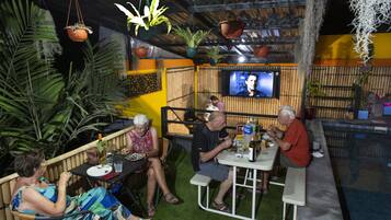 An outdoor dining area with tables and chairs, surrounded by potted plants and a bamboo fence.