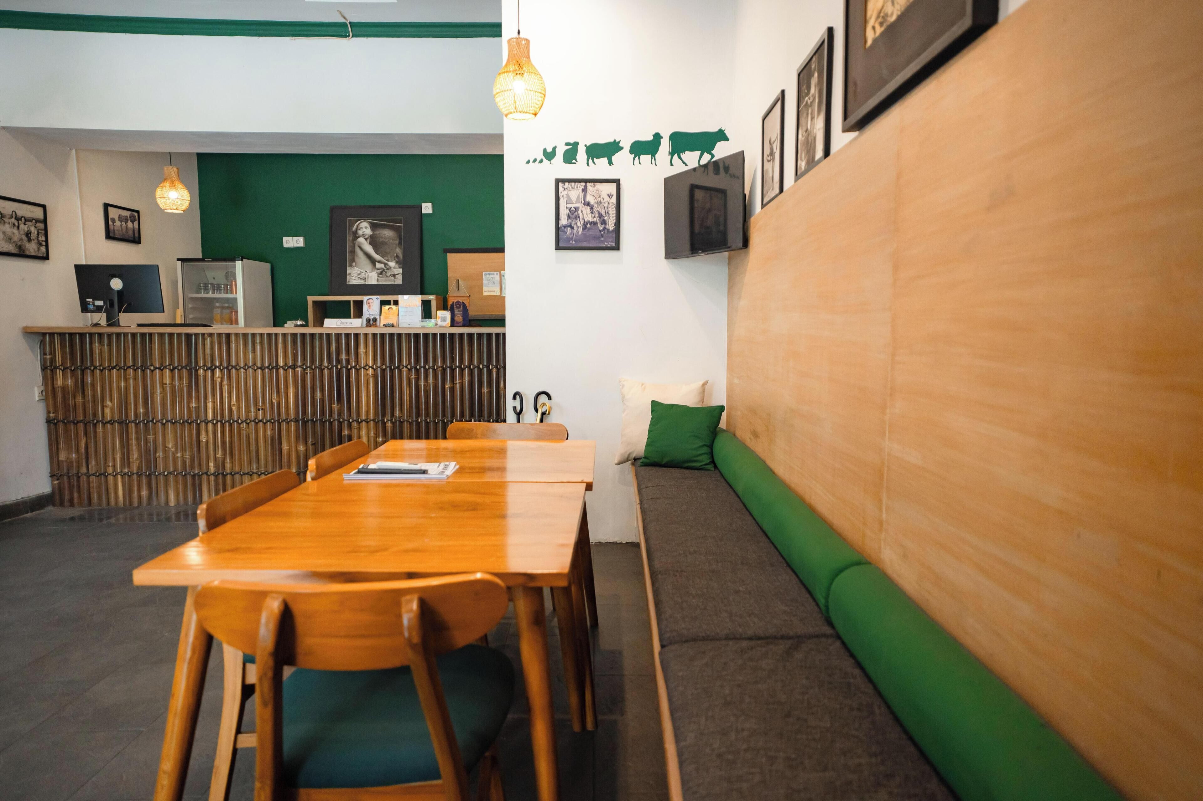 A restaurant with a wooden table and chairs, a green cushioned bench, and a bamboo partition in the background.