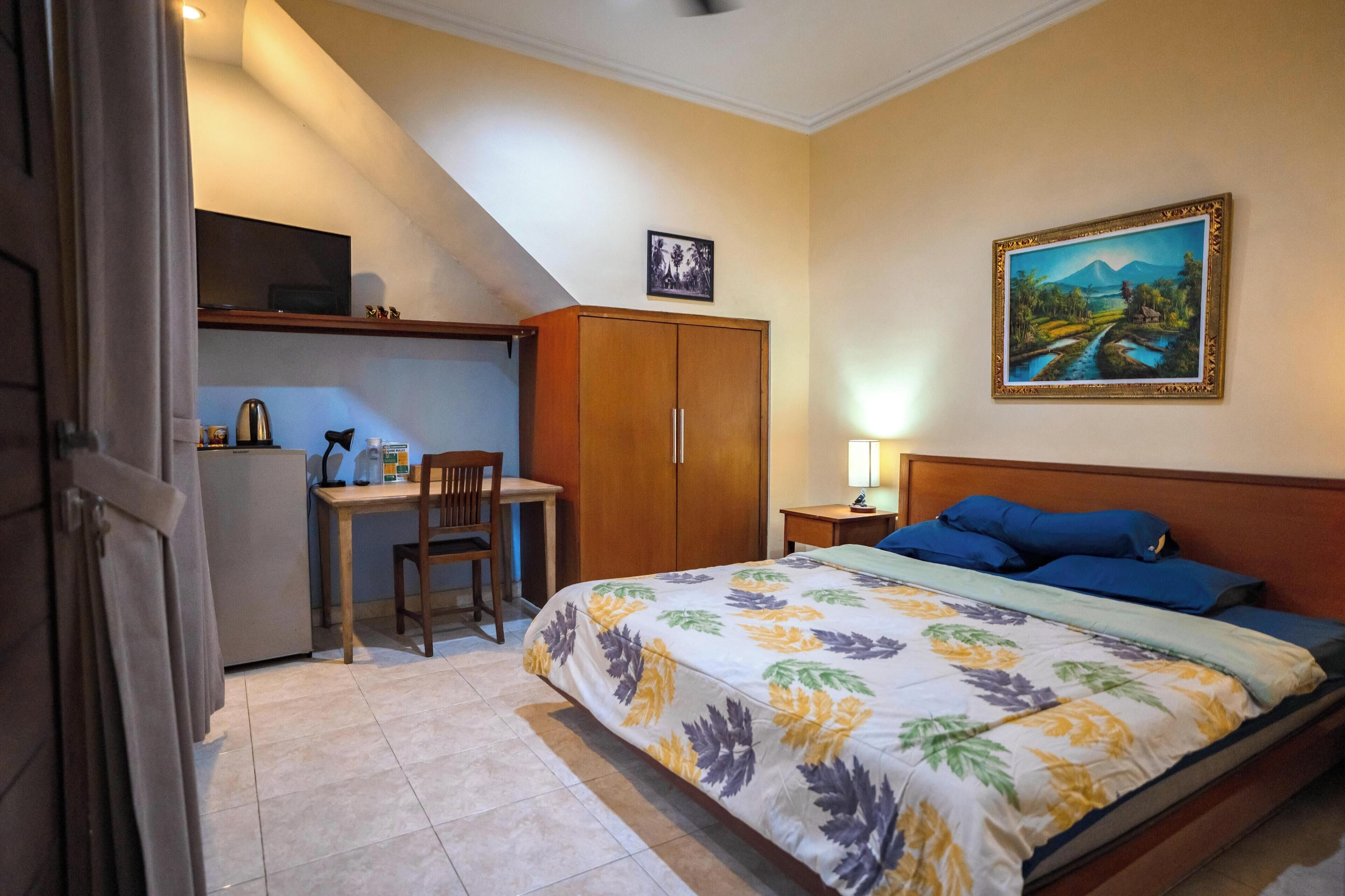 A bedroom with a bed, a desk, a chair, a wardrobe, and a painting on the wall.