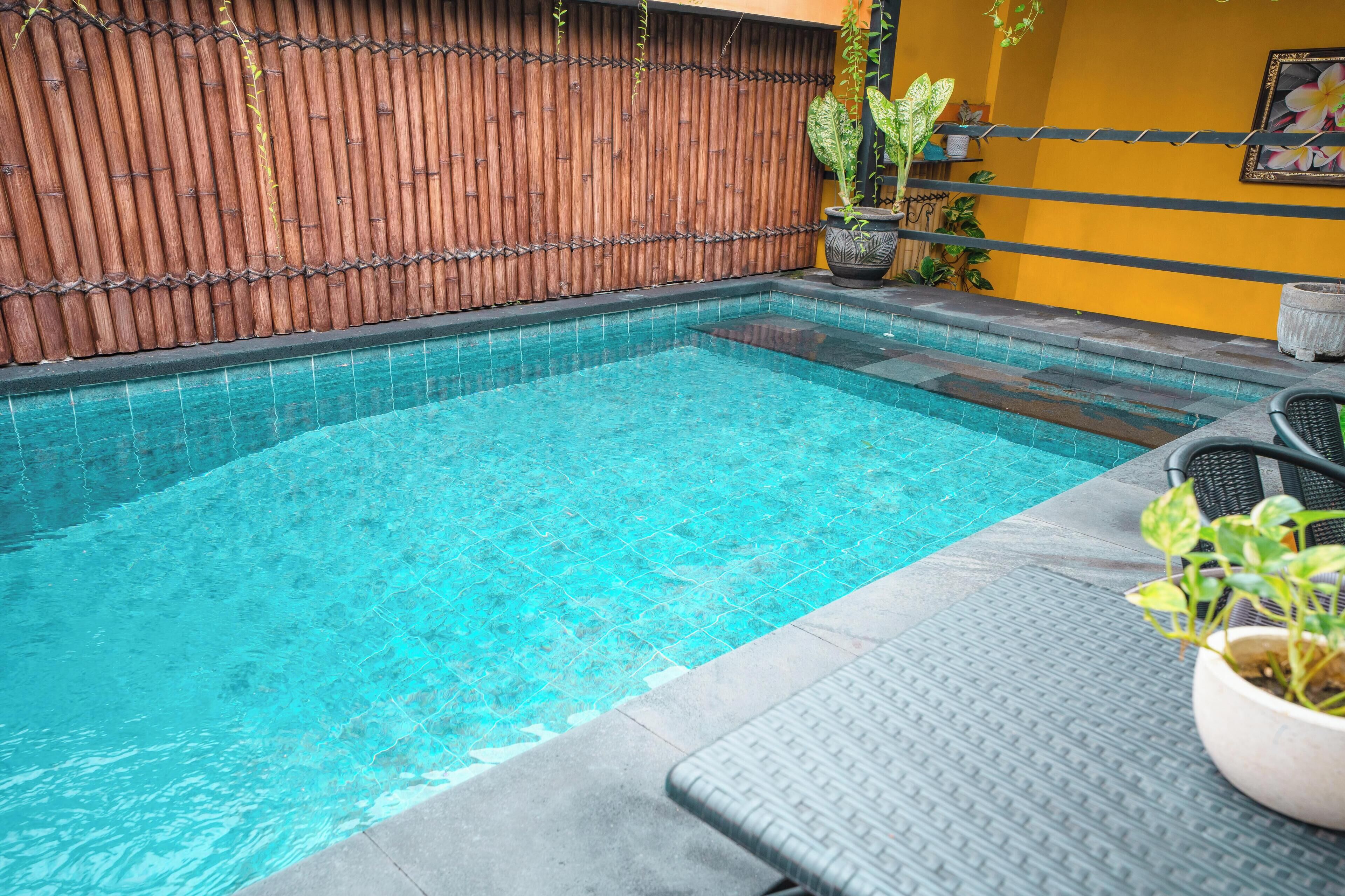 A swimming pool with clear blue water, surrounded by a bamboo fence and potted plants.