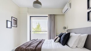 Une chambre d’hôtel avec un lit, une fenêtre avec des rideaux, un climatiseur fixé au mur et des tableaux encadrés accrochés au mur.
