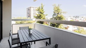 Un balcon avec une table et des chaises, un pot de fleurs et une vue sur des immeubles et des arbres.