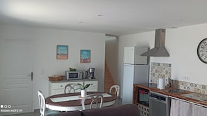 Una cocina compacta con microondas, cafetera y lavamanos. Hay una mesa de comedor con sillas y un reloj en la pared.